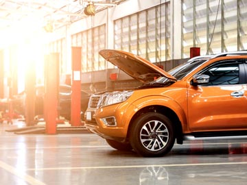 Ein orangefarbenes SUV steht in einer gut beleuchteten Auto-Werkstatt bei Autoankauf Geesthacht, dessen Motorhaube offen ist und den Motor zeigt.